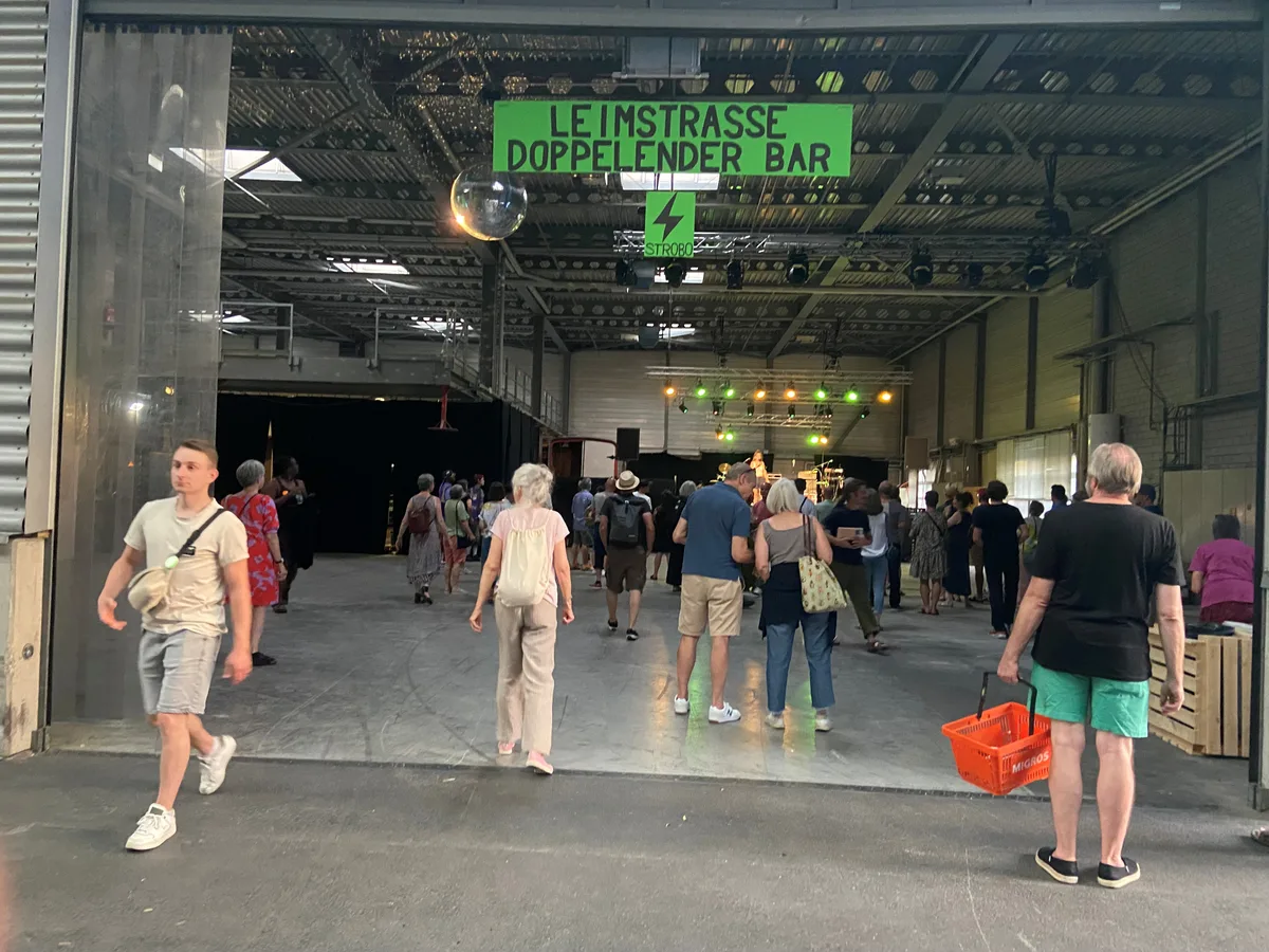 Menschen in einer Industriehalle, vorne steht eine Frau auf der Bühne.